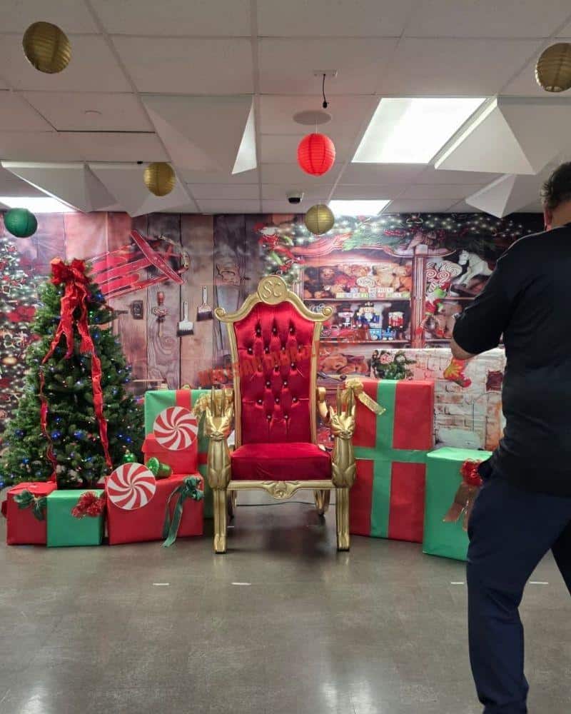 Santa photo session set in Dallas with a red and gold throne, peppermint gift boxes, a tree, and a photographer at the side.